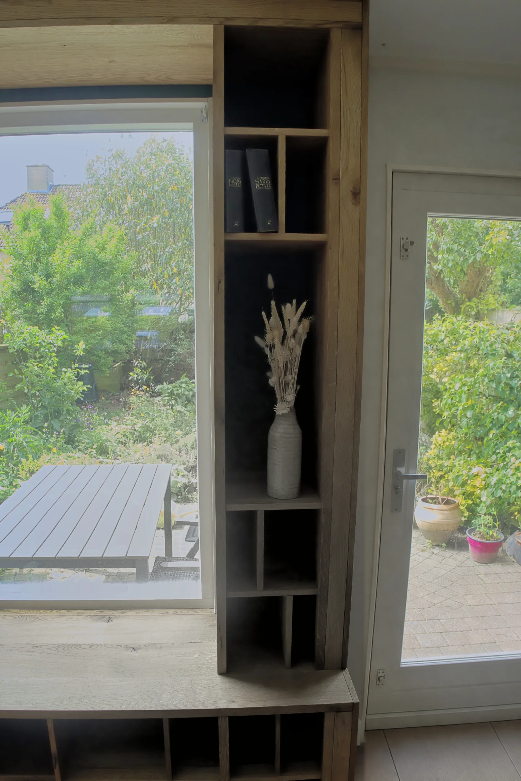 Detail van het rechter hoge kastdeel naast het raam, met boeken en een vaas in de vakken.