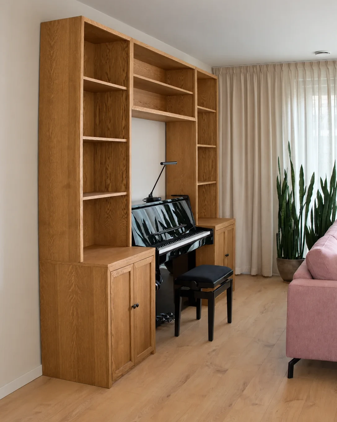 Eiken pianokast met open planken en paneeldeuren rond een zwarte piano.