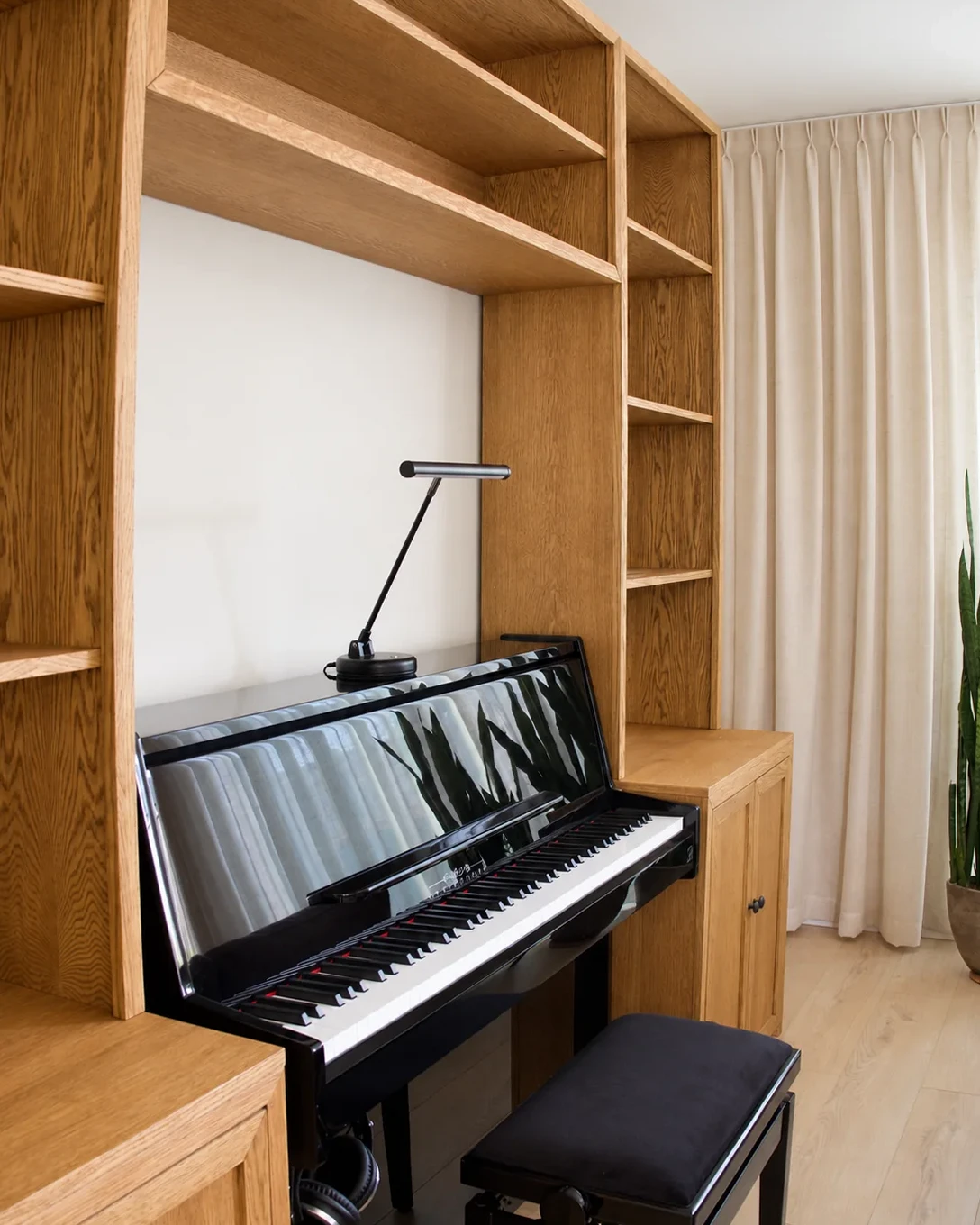 Zwarte piano tussen eiken kastdelen, met open planken erboven.