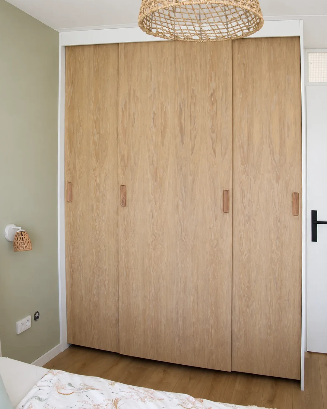 Kledingkast met gesloten deuren van eikenfineer en een wit kader in een slaapkamer.